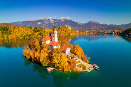 Foto de AERIAL: Stunning view of world renowned tourist attraction lake Bled with island. Gorgeous Bled island with church in embrace of vivid autumn trees. Beautiful fall season creating picturesque views. - Imagen libre de derechos