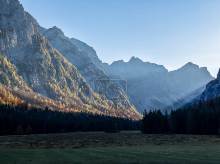 Téléchargez les photos : Golden glowing larch trees on mountain slopes above picturesque Krma Valley. Beautiful sun rays shining into the valley and illuminating steep mountainsides of Julian Alps coloured in autumn shades. - en image libre de droit