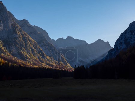 Foto de Picturesque view of Krma Valley and steep mountainsides with golden larch trees. Beautiful sun beams shining into the valley and illuminating mountain slopes of Julian Alps colored in autumn shades. - Imagen libre de derechos