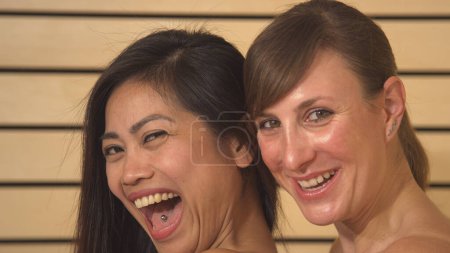 Foto de Beautiful head shot of cheerful and confident young ladies. Attractive Asian and Caucasian women posing and smiling for the camera before having a relaxing treatment in spa wellness - Imagen libre de derechos