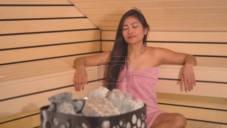 Photo for Heater stones in Finnish sauna with beautiful woman relaxing on bench. Sauna rocks as part of equipment for slower evaporation of sauna steam. Attractive lady treating herself in wellness. - Royalty Free Image