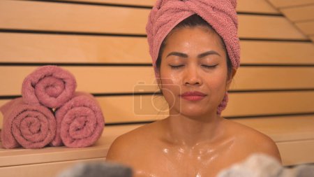 Foto de Face shot of Filipina with eyes closed sweating in hot Finnish sauna. Lady at sauna treatment for detoxification, stress relief and strengthening of the immune system in cold autumn months. - Imagen libre de derechos