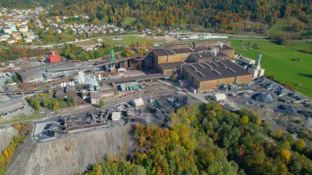 Téléchargez les photos : Industrial buildings and infrastructure for purpose of steel industry. Steel factory located by the river in picturesque valley surrounded with alpine landscape in colorful shades of autumn. - en image libre de droit