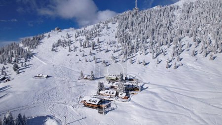 Téléchargez les photos : Snow-covered mountain chalets surrounded with snowy alpine ski resort. Hotel buildings in the middle of gorgeous alpine nature covered with newly fallen snow. Idyllic winter wonderland in Alps - en image libre de droit