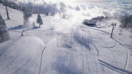 Téléchargez les photos : Ski area with working snow cannons for creating perfect skiing conditions. Snow preparation for consolidating snow base at ski slopes and a long winter season. Wintertime in mountain ski area. - en image libre de droit