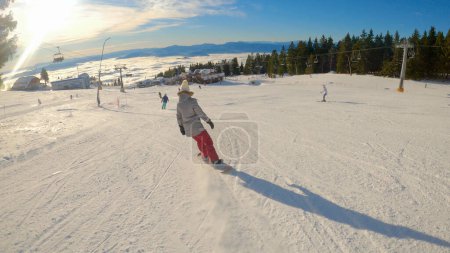 Photo for Young woman riding snowboard down the ski slope on a beautiful sunny winter day. Winter fairy tale for skiing and snowboarding in alpine ski resort. Female snowboarder enjoying at winter holidays. - Royalty Free Image