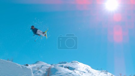 Téléchargez les photos : Male skier jumping big air kicker at snow park in snowy ski resort. Young extreme athlete flying above snow-capped mountaintops. Adrenaline activity on sunny winter day in ski resort. - en image libre de droit