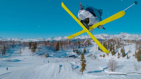 Stunning view of freestyle skier doing grab trick while jumping kicker. Young extreme athlete flying high above snow park and ski area. Adrenaline activity on sunny winter day in ski area.
