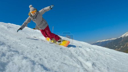 Photo for Young lady learning to ride a snowboard and making a turn on snowy ski slope. Female beginner snowboarder trying to keep balance while making a turn at snowboarding down the slope at ski resort. - Royalty Free Image