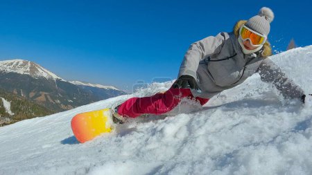 Téléchargez les photos : Young lady losing balance while learning a turn at snowboarding down the slope. Young female snowboarder tries to learn how to turn and ride snowboard at mountain ski resort on a beautiful sunny day. - en image libre de droit