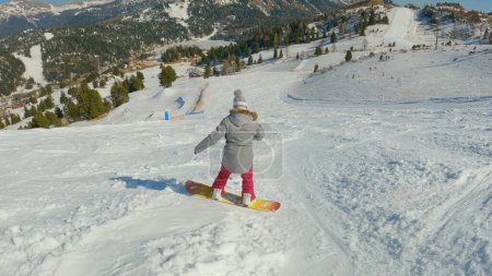 Photo for Young female learning to ride a snowboard and making turns on snowy ski slope. Girl snowboarder trying to keep balance while snowboarding and turning down the piste at snow-covered mountain ski resort - Royalty Free Image
