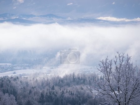 Photo for Remains of snowstorm clouds rolling over forested hilly countryside and villages. Magnificent hilltop view of beautiful rural landscape with snow-covered woodland and settlements after winter snowfall - Royalty Free Image