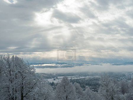 Téléchargez les photos : Sun rays shine through receding storm clouds rolling across snowy countryside. Incredible view from hilltop over hilly landscape covered with freshly fallen snow. Idyllic winter moment after snowstorm - en image libre de droit