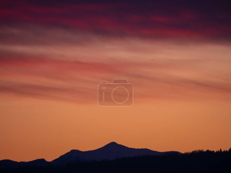 Téléchargez les photos : Magnificent view of glowing colorful sunset sky above snowy Sneznik mountain. Magnificent color shades of clouds at the end of the day. Stunning vista of vibrant atmospheric mood above mountains. - en image libre de droit