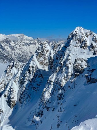 Téléchargez les photos : Gorgeous view of steep snow-covered mountain slopes and couloirs on a sunny day. Magnificent location for extreme adventures in pristine and untouched alpine terrains of snow-capped Albanian Alps. - en image libre de droit