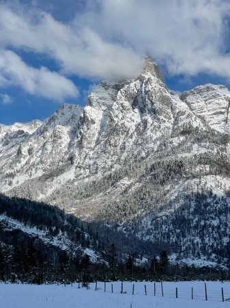 Foto de View from the valley to the majestic high mountain covered with fresh snow. White clouds gather around the snowy peak. Beautiful winter wonderland at remote high altitudes of wild Albanian Alps. - Imagen libre de derechos