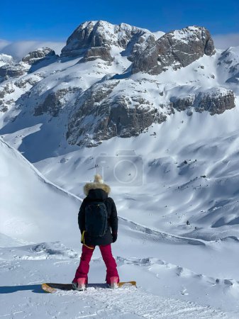 Photo for Sporty lady with snowboard checking line before riding on fresh powder snow. Magnificent views in pristine Albanian mountains and endless possibilities for snowboarding untracked mountain terrains. - Royalty Free Image