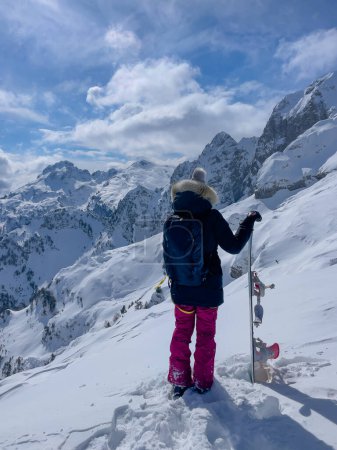 Téléchargez les photos : Lady holding snowboard on top of mountain slope and checking freeride lines. Endless possibilities for snowboarding freshly snowed and untracked terrains. Amazing views in pristine Albanian mountains. - en image libre de droit