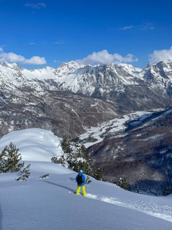 Téléchargez les photos : Male freerider with strapped snowboard admiring majestic view of snowy mountains. Male snowboarder before riding on fresh powder snow. Amazing winter scenery in pristine and wild Albanian Alps. - en image libre de droit