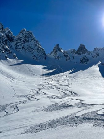 Téléchargez les photos : Winding tracks of skiers and snowboarders in powder snow on a mountain slope. Amazing travel destination for adventurous heliboarding and heliskiing in pristine and freshly snow-covered Albanian Alps. - en image libre de droit