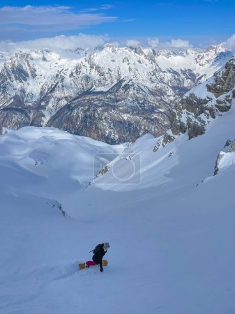 Foto de Snowy mountainside with stunning view and snowboarder descending on fresh powder. Gorgeous travel destination for adventurous heliboarding and heliskiing in pristine and snow-covered Albanian Alps. - Imagen libre de derechos