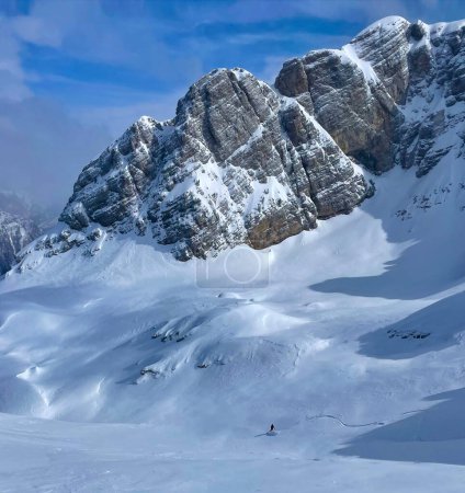 Téléchargez les photos : Snowboarder riding down on powder snow under snow-covered mountain peaks. Picturesque travel destination for adventurous heliboarding and heliskiing in pristine and untracked terrains of Albanian Alps - en image libre de droit