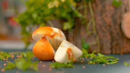 Téléchargez les photos : MACRO, DOF: Fragrant quartered onion falls onto the black kitchen counter next to tiny seeds. Small mustard seeds and green herbs scatter across the table as a half peeled onion comes falling down. - en image libre de droit