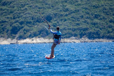 Téléchargez les photos : CLOSE UP, DOF : Une jeune femme détendue surfe vers le littoral méditerranéen par une journée d'été ensoleillée. Surfeuses touristiques méconnaissables sur une planche de papier d'aluminium vers la péninsule intacte de Peljesac. - en image libre de droit
