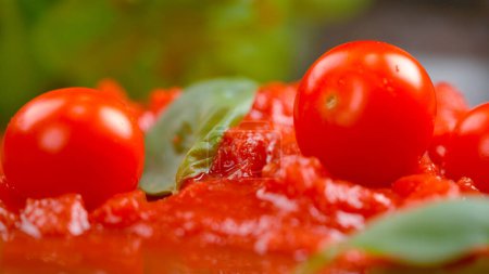 Téléchargez les photos : MACRO, DOF: Small cherry tomatoes fall into the fresh vegetarian tomato sauce with fragrant basil. Detailed view of shiny round tomatoes resting in freshly made marinara sauce sitting in a plate. - en image libre de droit
