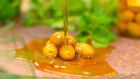 Photo for DOF, MACRO: Extra virgin olive oil is poured over the cured olives sitting on the cold stone countertop. Golden cold pressed olive oil splashes over a pile of homegrown olives. Tasty oil and olives. - Royalty Free Image