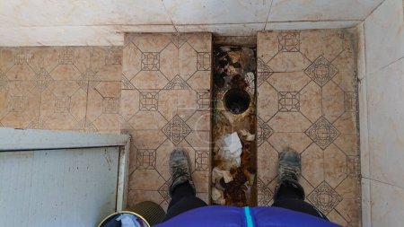 Foto de POV: De pie sobre una letrina sucia en cuclillas en un baño apestoso en el Tíbet. Los viejos excrementos humanos están llenando el asqueroso retrete de letrinas. El viajero se para sobre un baño público de pesadilla. - Imagen libre de derechos