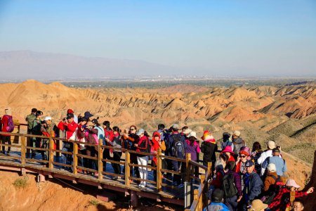 Photo for RAINBOW MOUNTAINS, CHINA; OCTOBER 2018: Masses of tourists move along the wooden walkway with a stunning view of the famous Rainbow Mountains. Hordes of travelers fill up a geological park in Zhangye. - Royalty Free Image