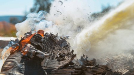 Photo for MACRO, DOF: A pile of carton burning in the backyard is extinguished by the white fire extinguisher foam. Heap of waste paper burning in sunny outdoors is put out by a portable fire extinguisher. - Royalty Free Image