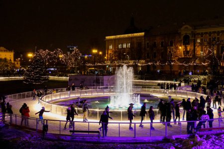 Téléchargez les photos : ZAGREB, CROATIE, DÉCEMBRE 2018 : Des touristes joyeux patinent autour d'une fontaine dans un parc de Noël à Zagreb. Enfants et adultes s'amusent à explorer la foire du Nouvel An en Croatie le soir parfait. - en image libre de droit