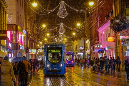 Téléchargez les photos : ZAGREB, CROATIE, DÉCEMBRE 2018 : FERMER : Par une froide nuit d'hiver, le tramway traverse une rue festive de Zagreb. Les touristes et les habitants aiment explorer la ville européenne pittoresque en hiver. - en image libre de droit