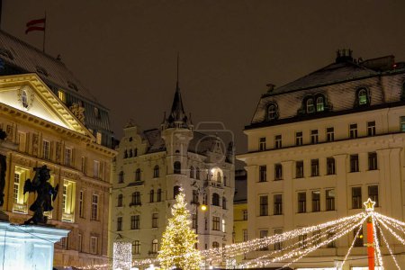 Photo for CLOSE UP: Christmas lights and ornaments light up the historic buildings in Vienna. Picturesque view of old European architecture during the winter holidays. Buildings above idyllic advent market. - Royalty Free Image