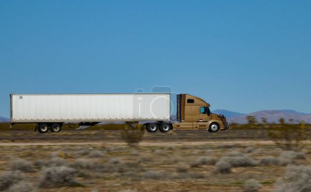 Téléchargez les photos : FERMER : Camion semi-remorque couleur or vitesses le long de la route inter-États traversant un désert aux États-Unis. Camion transporte des conteneurs de fret lourd à travers la campagne des États-Unis d'Amérique - en image libre de droit