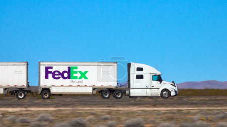 Téléchargez les photos : UTAH, ÉTATS-UNIS D'AMÉRIQUE, MARS 2019 : FERMER : FedEx accélère le long d'une autoroute interétatique traversant le vaste désert de l'Utah. Service de livraison camion semi-remorque traverse le paysage stérile. - en image libre de droit