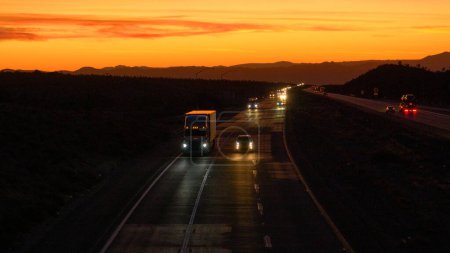Photo for DRONE: Commuters and truckers drive down the famous Mojave freeway at scenic twilight. Picturesque golden evening sky gently illuminates the highway leading traffic across the rugged Mojave desert. - Royalty Free Image