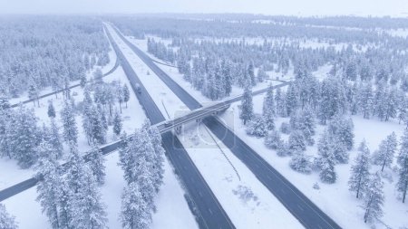 Foto de AERIAL: Escénica vista del paisaje nevado blanco que rodea una concurrida carretera interestatal en Washington, Estados Unidos. Volando por encima del tráfico conduciendo a lo largo de una carretera de asfalto resbaladiza cruzando los bosques nevados - Imagen libre de derechos