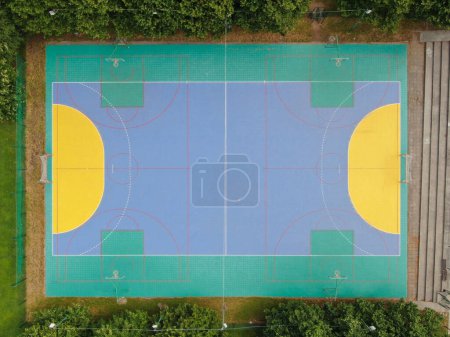 Photo for AERIAL, TOP DOWN: Flying away an empty colorful multi sport court near a high school. Cool aerial view of handball goals and basketball backboards around multi colored playground in empty sports park. - Royalty Free Image