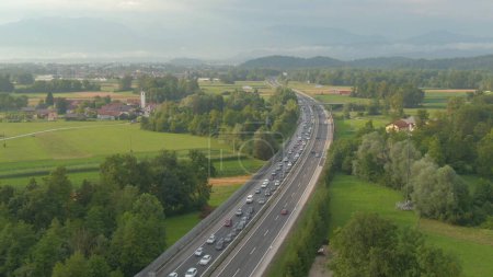 Photo for AERIAL: Flying along a long traffic jam formed on an asphalt highway crossing the idyllic green countryside. Countless commuters and tourists get caught in a congestion caused by a car accident. - Royalty Free Image