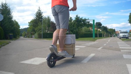 Photo for CLOSE UP: Delivery guy rides an electric scooter down sidewalk with two packages - Royalty Free Image
