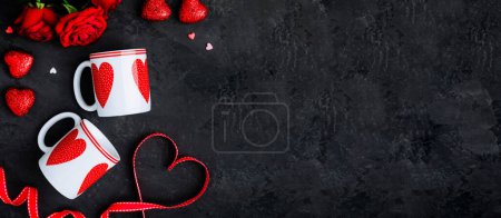 Photo for Valentine's Day table setting with two cups, red ribbon and hearts on dark background, top view, copy space. Valentines day background, holiday concept. - Royalty Free Image