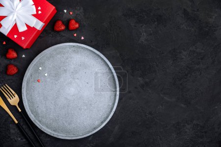 Photo for Valentine's Day table setting with empty plate, red hearts and present box on dark background, top view, copy space. Valentines day background, holiday concept. - Royalty Free Image