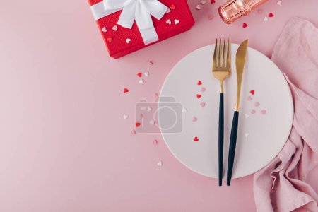 Photo for Valentine's Day background. A set of golden cutlery and pink napkin on plate with hearts confetti. Top view, copy space. - Royalty Free Image