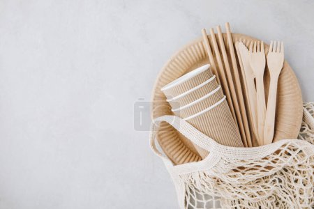 Photo for Disposable paper tableware (paper cups, plates, straws, wooden forks, knives, ) on gray stone background, top view, copy space. Plastic free and zero waste concept. - Royalty Free Image