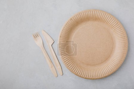 Photo for Disposable paper tableware (paper plates, wooden forks, knives, ) on gray stone background, top view, copy space. Plastic free and zero waste concept. - Royalty Free Image
