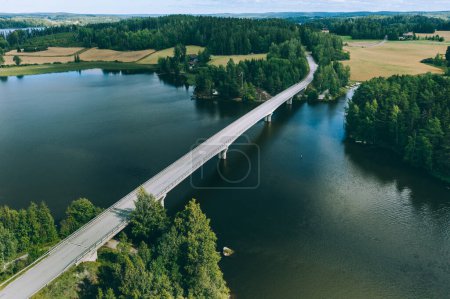 Photo for Aerial view of road bridge over blue lake water and green woods in Finland. Beautiful summer landscape. - Royalty Free Image