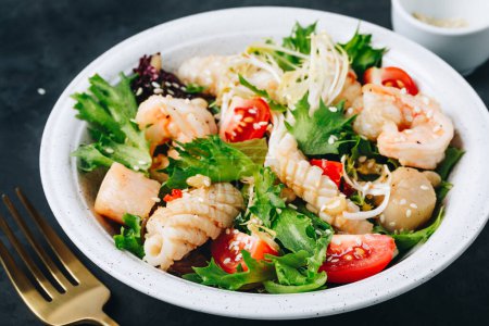 Photo for Seafood salad bowl. Green lettuce tomato salad with shrimps, scallop and squids on dark background - Royalty Free Image
